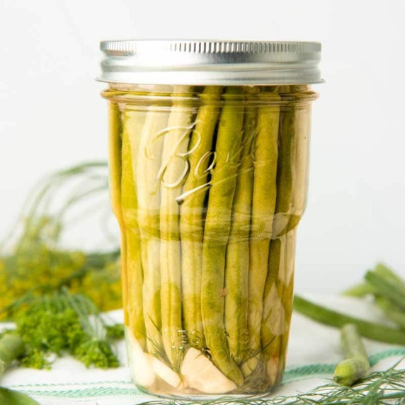 Close up of canned dilly beans in a Ball Nesting Jar with fresh dill and green beans around it.