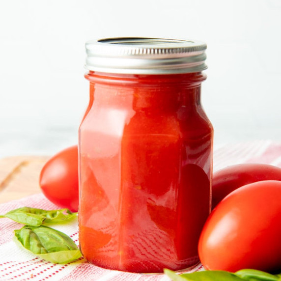 A jar of canned tomato sauce stands with fresh tomatoes and basil around it.