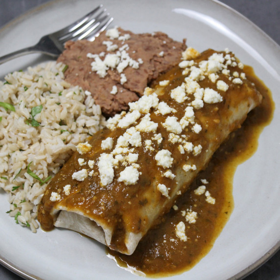 A restaurant style carnitas burrito with verde sauce and queso fresco