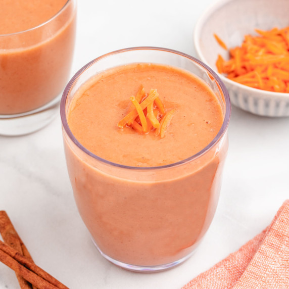 A banana and carrot smoothie in a glass with shredded carrots on top.