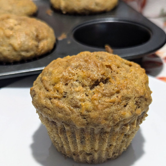 A carrot muffin in front a muffin pans with more muffins in it. 