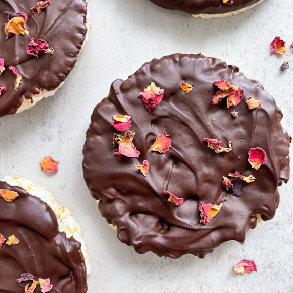 Chocolate coated rice cakes sprinkled with dried rose petals on a light grey table 