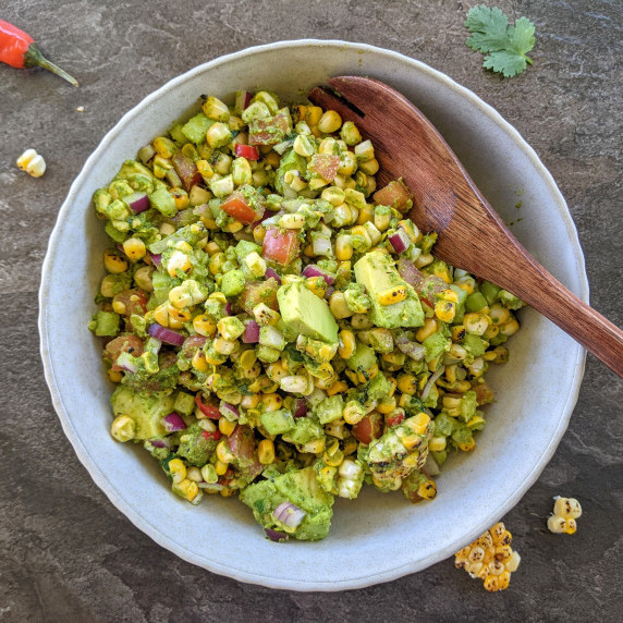 Charred corn salad in a cream bowl with a wooden salad spoon. The bowl is on a granite countertop. 