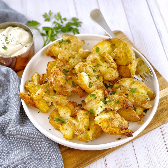 crispy baby potatoes on a white plate with a fork and creamy sauce in a pot on the side