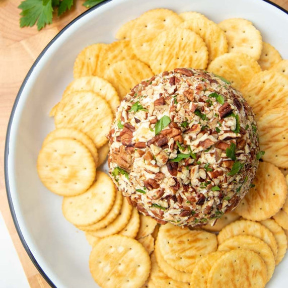 Top view of a cheese ball appetizer crusted in pecan pieces on a platter surrounded by crackers.
