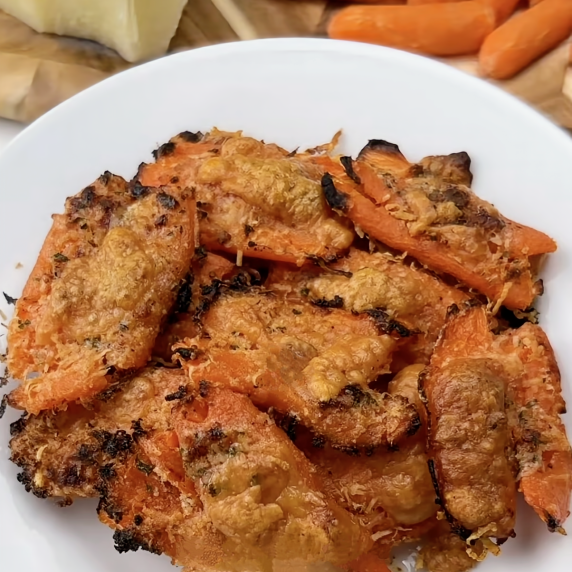 Crispy smashed carrots on a plate with a block of cheese and whole carrots in the background.