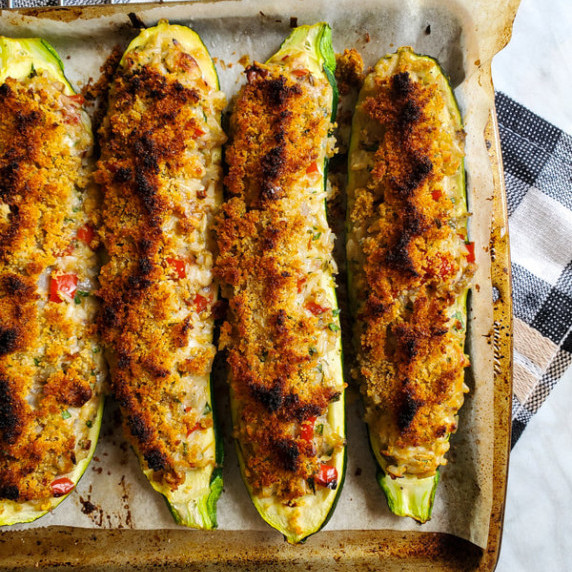 A parchment lined tray with cheesy, stuffed zucchini topped with crumbs.