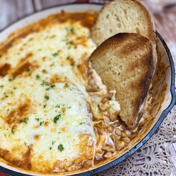 Cheesy bean and tomato bake in a skillet with grilled bread dunked on the side.