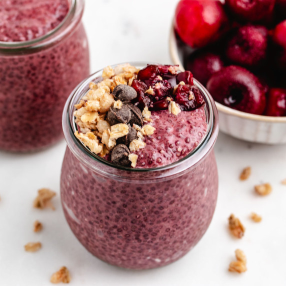 Cherry chia pudding in a glass jar with granola, chocolate chips, and diced cherries on top.