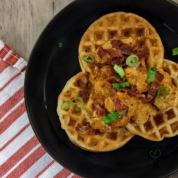 A plate of fried chicken and waffles topped with bacon and scallions