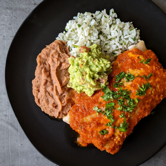 A wet burrito smothered in ranchero sauce served with rice, beans, and a scoop of guacamole