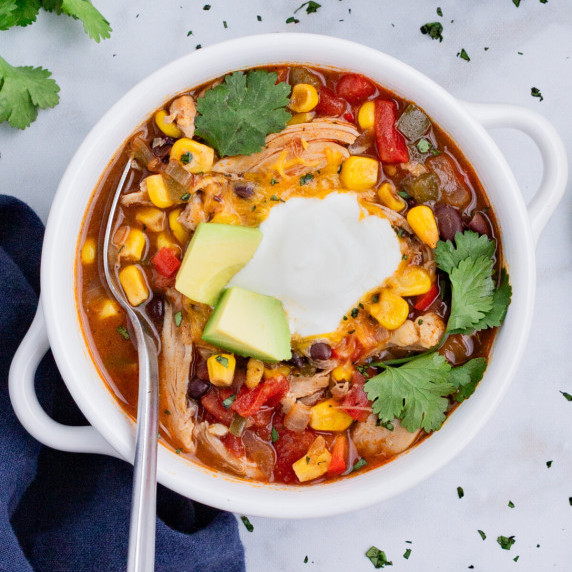 Chicken Enchilada Soup RECIPE served in a white soup bowl garnished with avocados and sour cream.