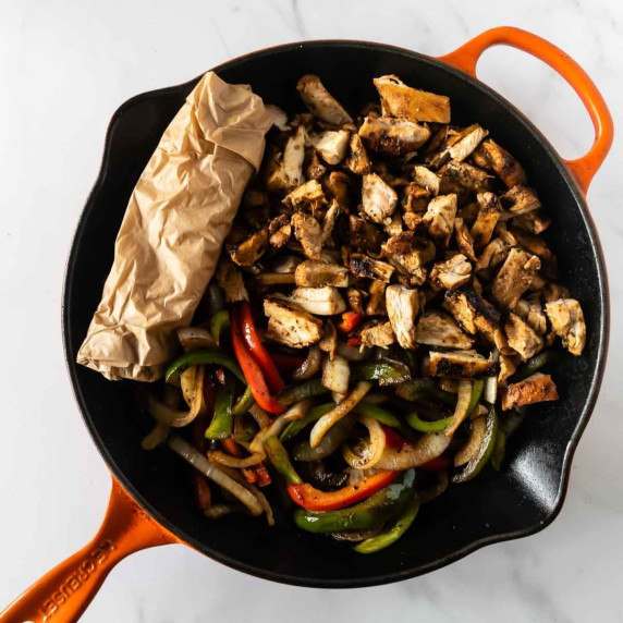 chicken fajitas in a cast iron skillet with tortillas rolled in parchment paper.