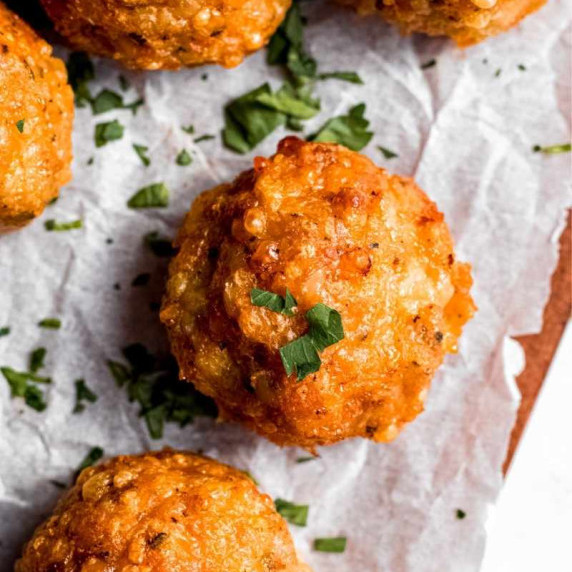 Close view of baked chicken meatballs on parchment paper garnished with minced fresh herbs.