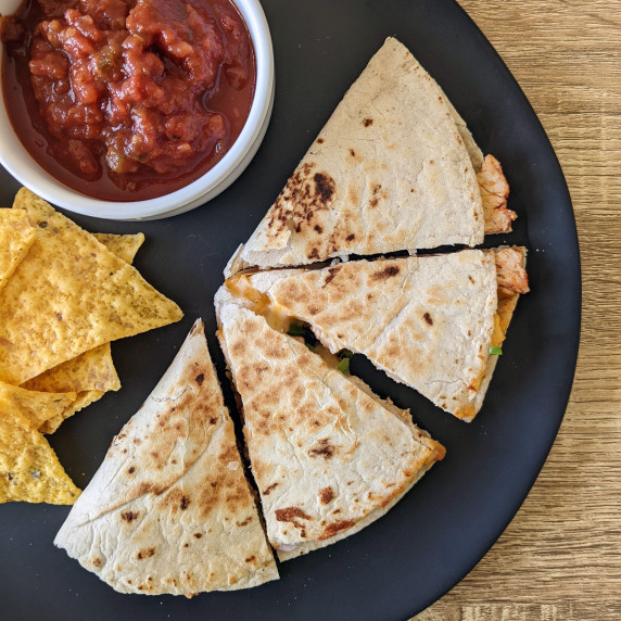 Four quesadilla triangles on a plate with chips and salsa