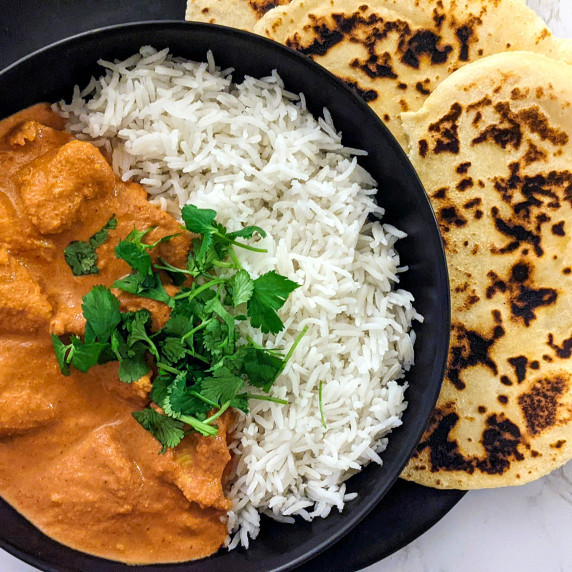 A bowl of creamy chicken tikka masala with basmati rice and naan on the side