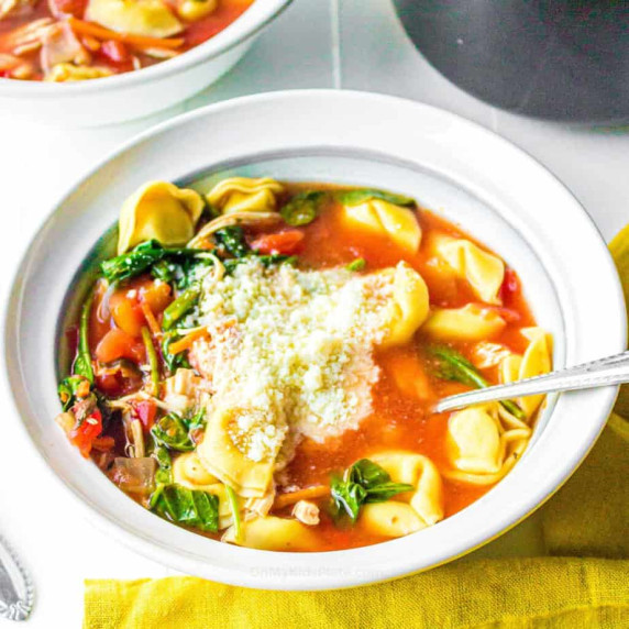 A bowl of tomato soup with tortellini, spinach and cheese.