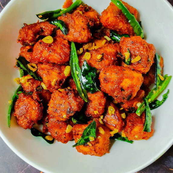 Deep fried crispy chicken 65 pieces tempered with curry leaves and garlic, served in a white dish