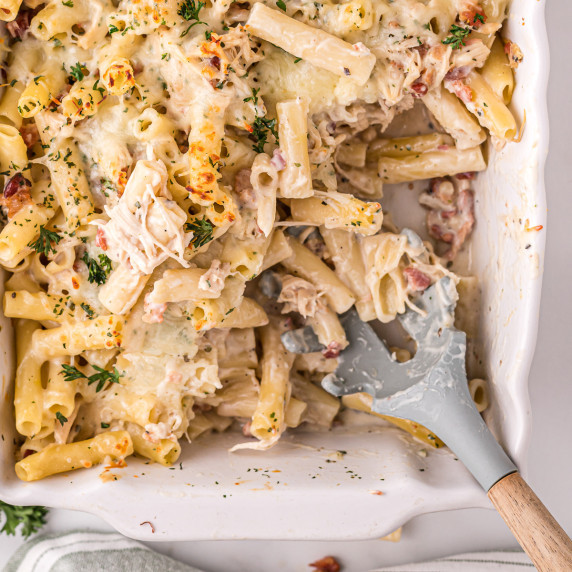 Pasta casserole with chicken, bacon, cheese, and parsley. Serving spoon is resting in the dish
