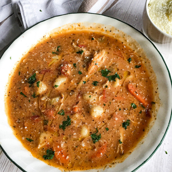 Chicken gnocchi soup in a bowl with fresh vegetables and topped with parsley and Parmesan cheese. 