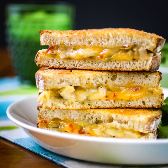 Side shot of three halves of grilled cheese sandwiches stacked on each other on a white plate.