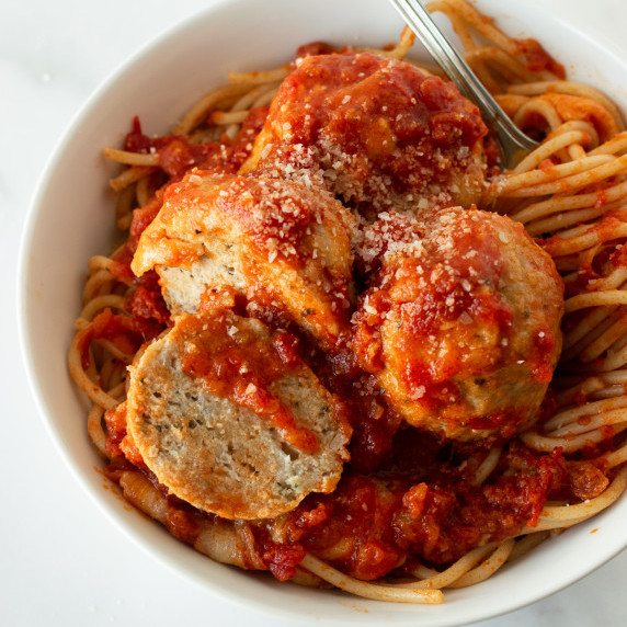 chicken parmesan meatballs in a white bowl with spaghetti and a fork.
