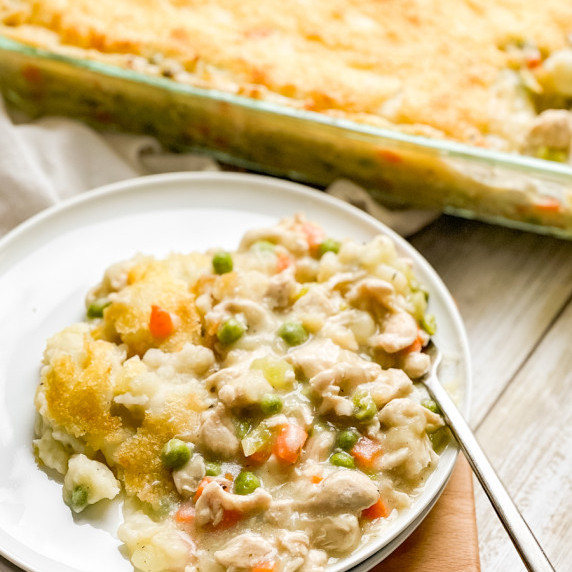 A round white plate in the foreground with the chicken pot pie and a fork on it. 