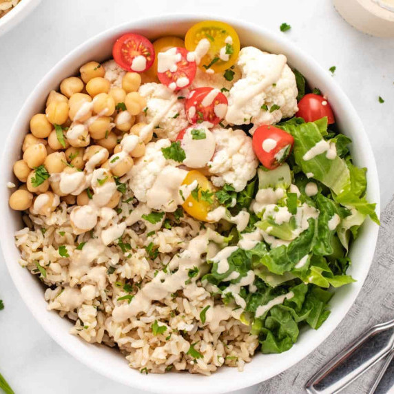 Brown rice, chickpeas, cauliflower, cherry tomatoes, and lettuce in a white bowl.