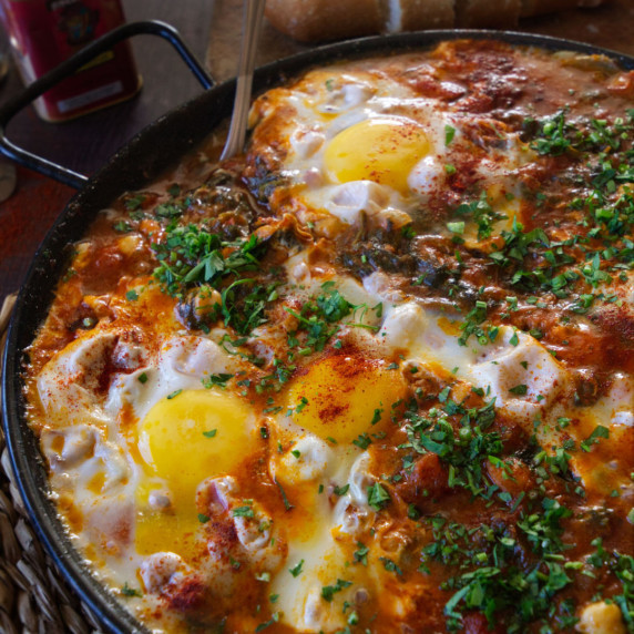 a large pan of chickpeas, spinach, and eggs sits on a table waiting to be served. 