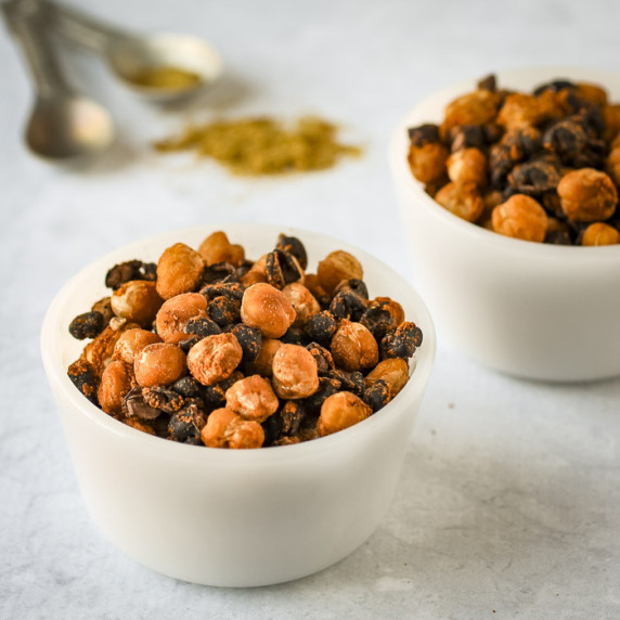 Side shot of two white bowls of chickpeas and black beans with spices and measuring cups in the back