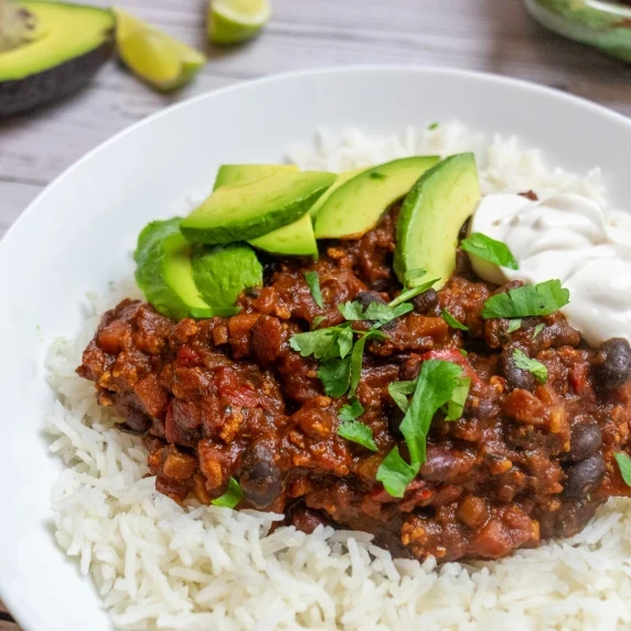 Side on shot of vegan chili with avocado and lime in the background