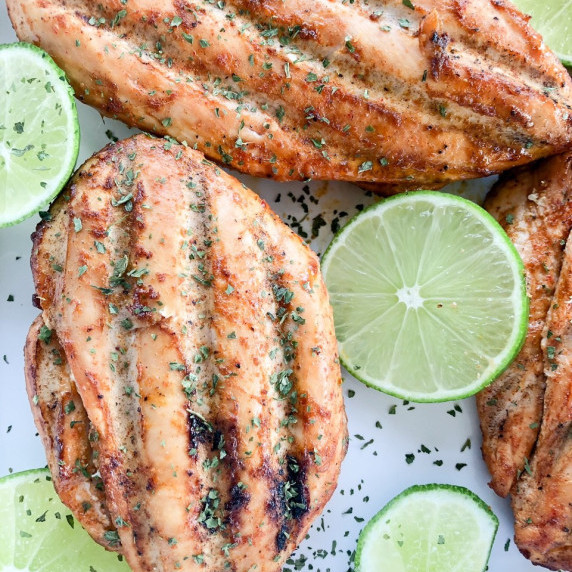 Chili lime chicken breasts arranged on a white platter with slices of fresh lime