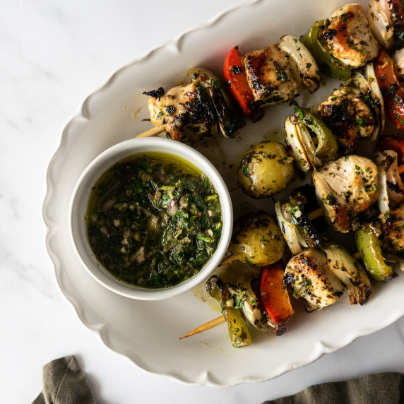 chimichurri chicken kabobs on a white platter with chimichurri sauce.