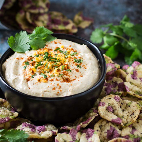 Side angled shot of cheddar cheese dip garnished with herbs and cayenne in a black bowl.