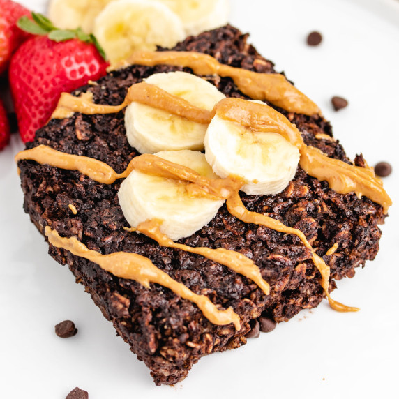 Chocolate baked oatmeal slice on a plate with peanut butter and banana slices.