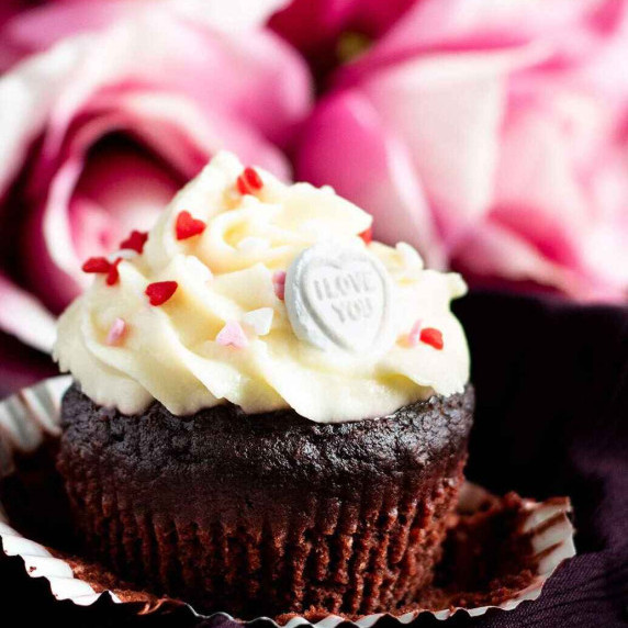 A chocolate and beetroot cupcake in front of pink roses.