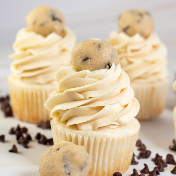 Vanilla cupcakes with piped chocolate chip cookie dough buttercream frosting and round dough balls.