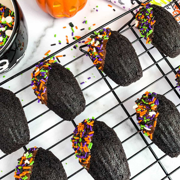 Chocolate Madeleines with Halloween sprinkles on a black cooling rack.