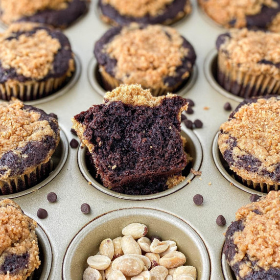 Chocolate peanut butter muffins in a pan with peanuts and chocolate chips sprinkled on top.