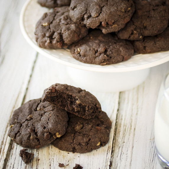 Side shot of multiple chocolate cookies stacked on a white serving platter and a wooden surface.