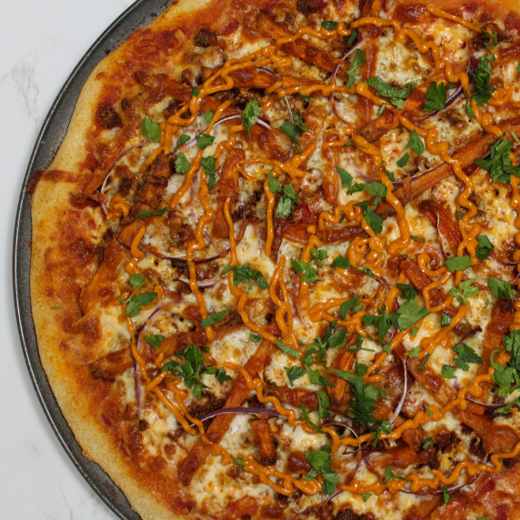 A pizza topped with chorizo, red onion, sweet potato fries, chipotle mayo, and fresh cilantro