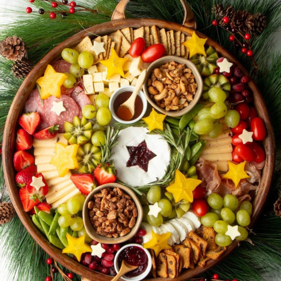 A round tray arranged to look like a christmas wreath with cheese, meat, crackers, fruits, and nuts.