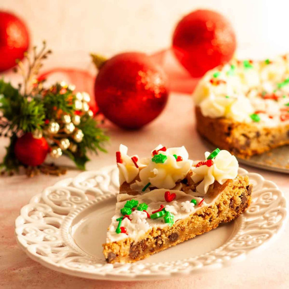 A slice of Christmas cookie cake on a white plate next to ornaments.