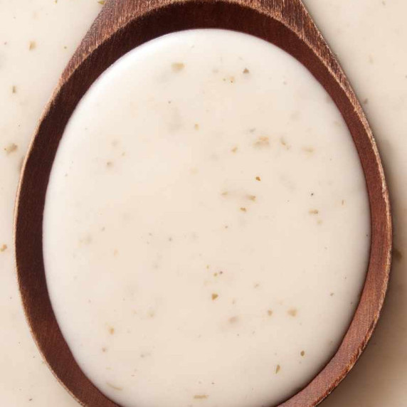 Close view of homemade caesar salad dressing in the center of a wooden spoon.