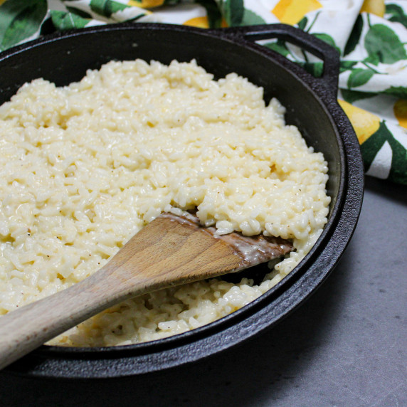 A cast iron pan of creamy parmesan risotto with a wooden spatula