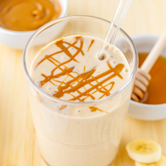 Close-up of peanut butter banana smoothie with a glass straw and peanut butter drizzle on top.