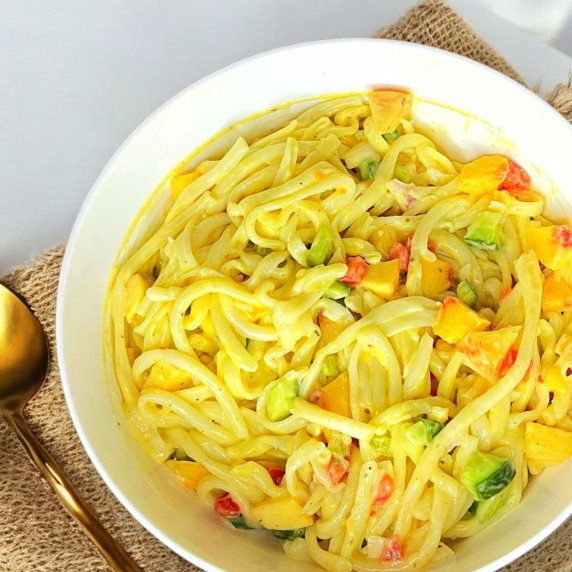 Cold noodle salad with loads of fruits and veggies in zesty sauce served in a white bowl.