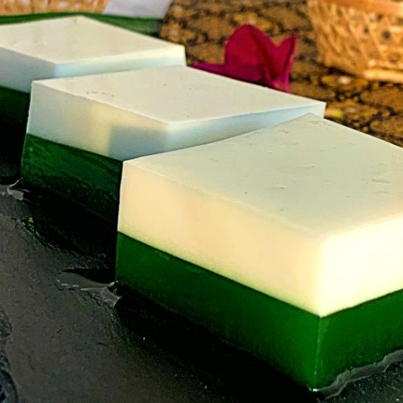3 square parts of Thai pandan coconut jelly in a row. The top layer is white and the bottom is green