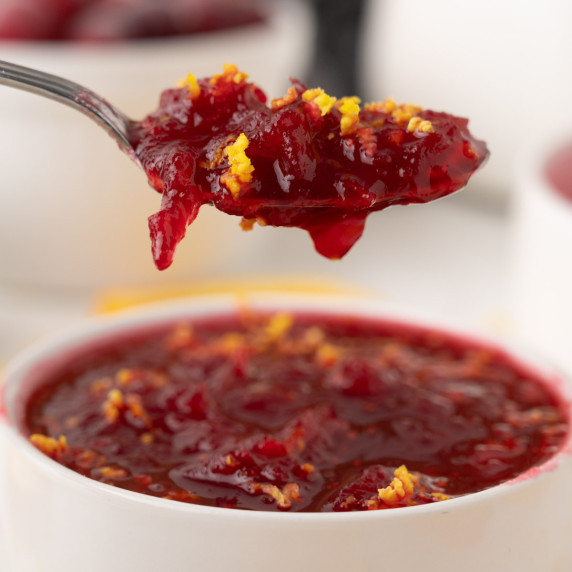 Cranberry sauce in white ramekin with spoon full above.
