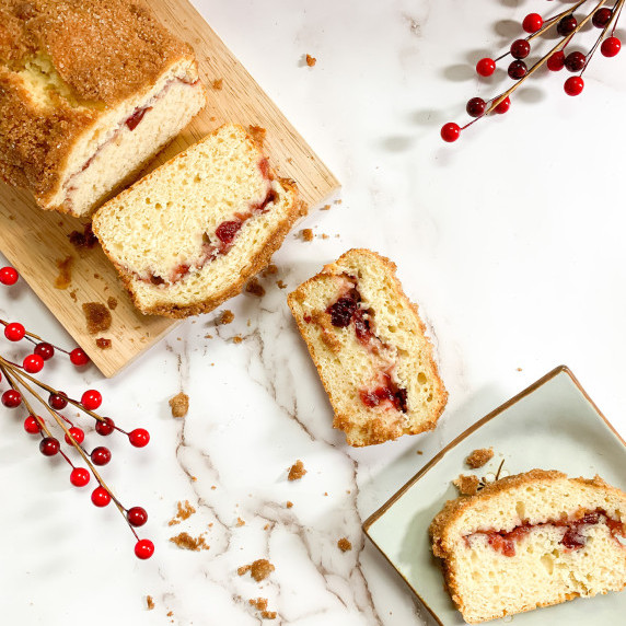 Cranberry coffee cake sliced with pieces on the counter and one on a light blue plate